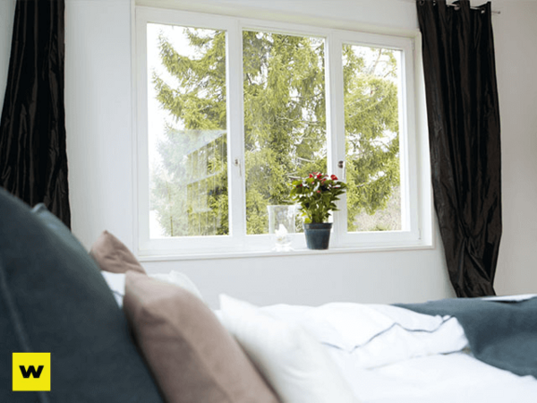 Helles Schlafzimmer mit großem Fenster, Blick ins Grüne und Zimmerpflanze auf der Fensterbank.