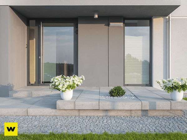 Moderner Hauseingang mit großen Glasflächen, Pflanzkübeln und gepflegter Steinplatte.