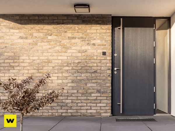 Moderne Haustür aus Aluminium neben heller Klinkerfassade mit Pflanze im Eingangsbereich.