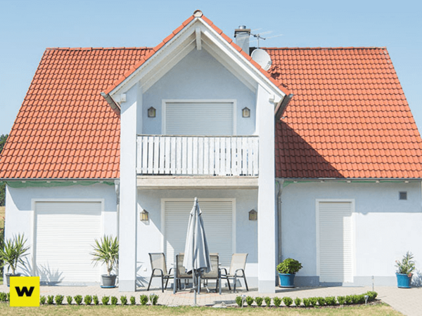 Modernes Einfamilienhaus mit rotem Ziegeldach, Terrasse und Garten bei Sonnenschein.